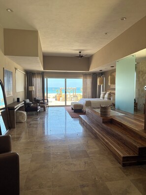 A spacious room with a large bed, a wooden bench, a seating area, and a view of the beach.