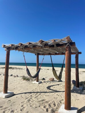A wooden beach structure with a woven roof and two hammocks.