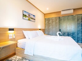 A hotel room with a bed, a nightstand, a wall-mounted air conditioner, and a painting above the bed.