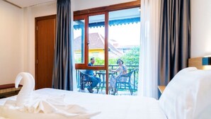 A hotel room with a bed, a swan-shaped pillow, a balcony with two chairs, and a view of a building and greenery. - New Champa Boutique Hotel (Vientiane)