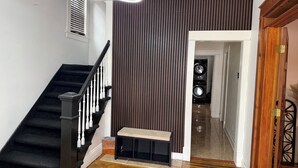 A staircase with black railings and white balusters, a bench, a wall with vertical slats, and a door leading to another room. - Colonial Style Home 5 Br 2 bath n’ Parking! Close to restaurants n’ colleges! (Albany)