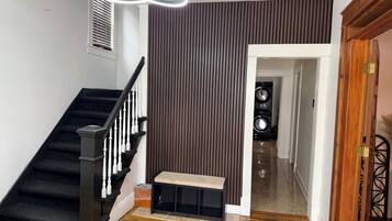 Un escalier avec des rampes noires et des balustrades blanches, un banc, un mur avec des lattes verticales et une porte donnant sur une autre pièce.
