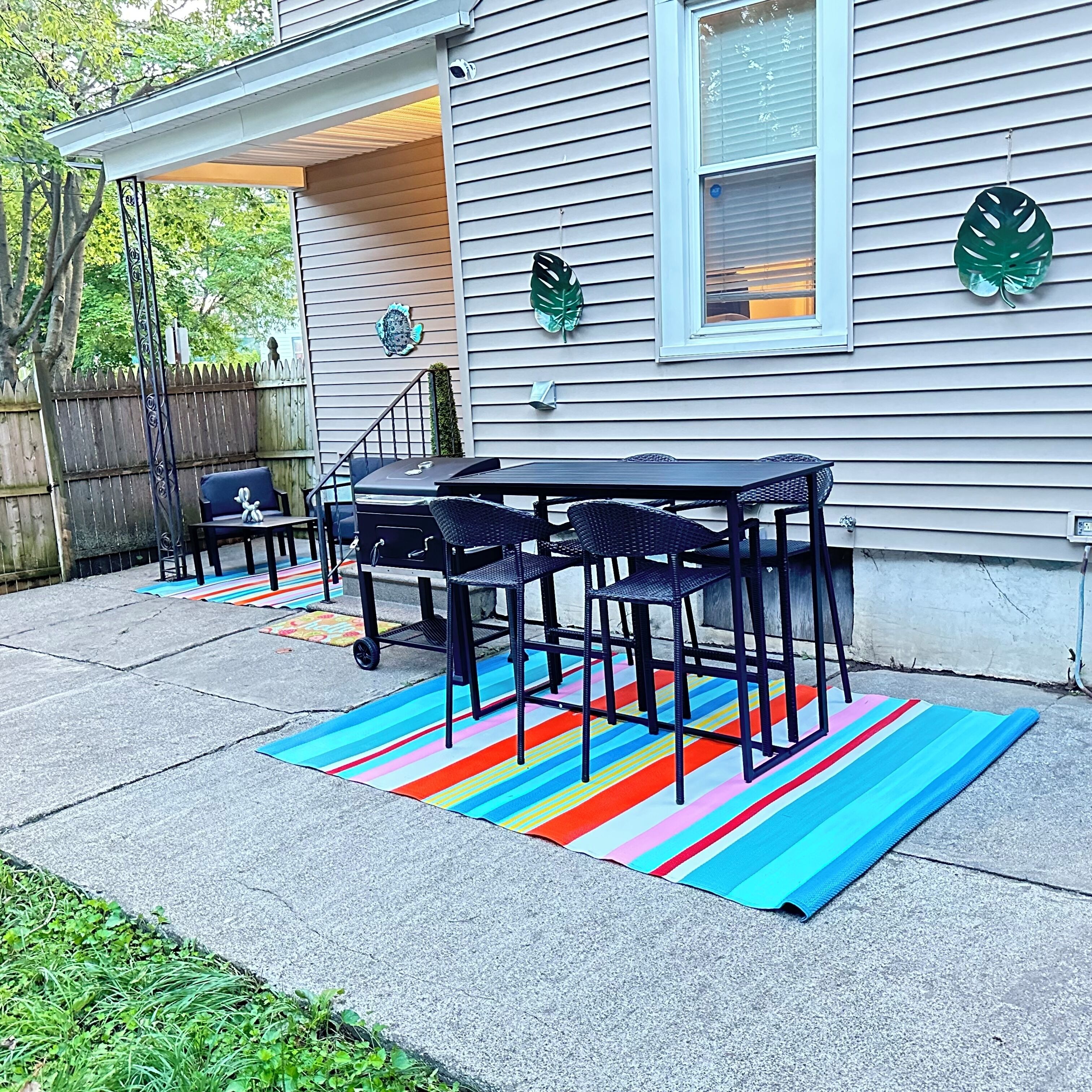 A patio with a table and chairs, a grill, and a colorful striped rug.