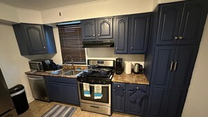 A kitchen with dark blue cabinets, a stainless steel stove, a microwave, and a coffee maker. - Colonial Style Home 5 Br 2 bath n’ Parking! Close to restaurants n’ colleges! (Albany)