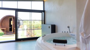 A modern bathroom with a large bathtub, a wooden barrel structure outside the window, and a view of the outdoors. - Burgemeestershof (Wetteren)