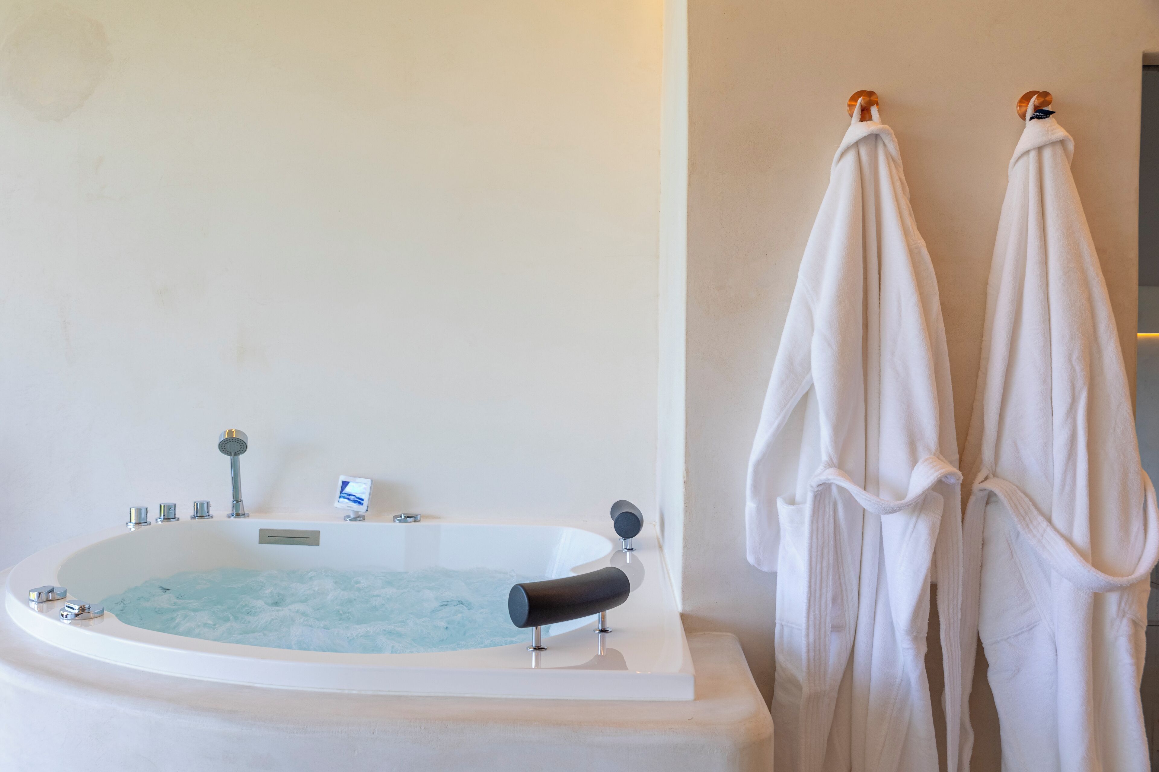 A large bathtub with a control panel, two towels hanging on hooks, and a small shelf with a bottle.