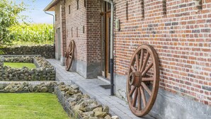 A brick building with large wooden wheels attached to the exterior wall, a stone wall, and a grassy area with a metal fence. - Burgemeestershof (Wetteren)