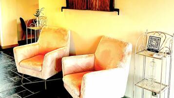 A room with two plush armchairs, a wooden wall art piece, a small table with a vase, and a metal shelf with a QR code.