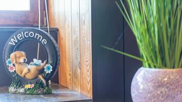 Welkomstbord met een hond en bloemen, houten wand en een bloempot.