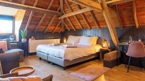 A bedroom with a sloped ceiling, a bed with white bedding, a bedside table with a lamp, a chair, and a window with a view. - Burgemeestershof (Wetteren)