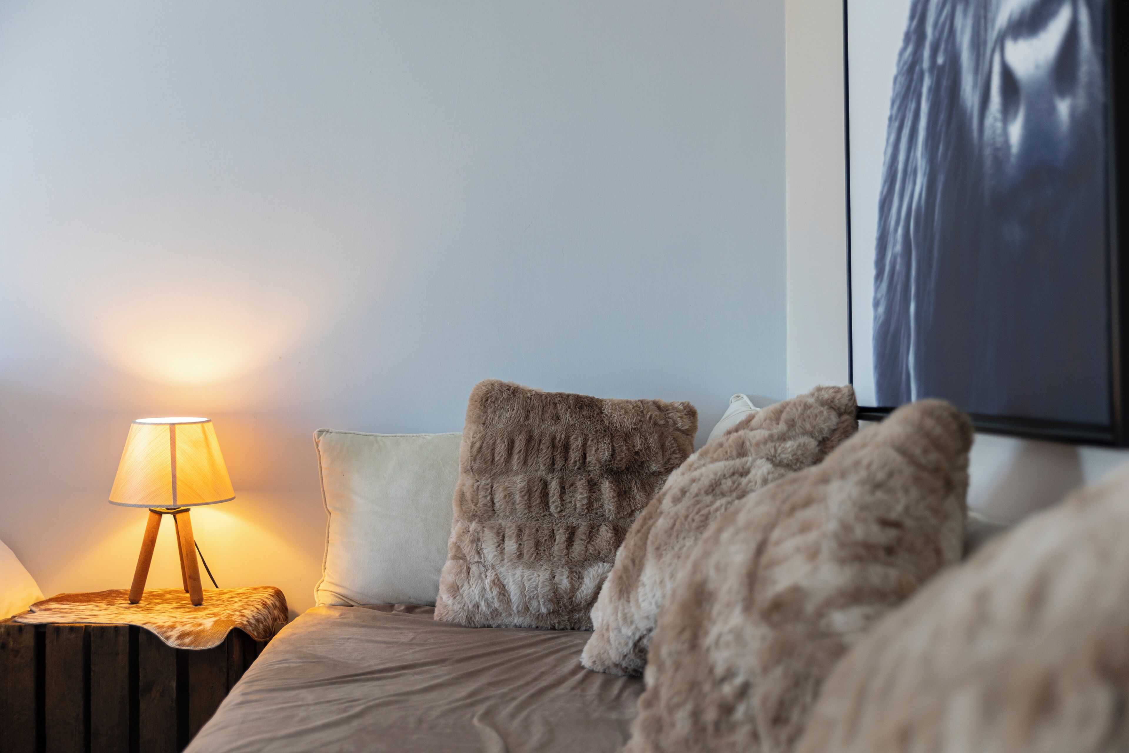 A bedroom with a bed, a nightstand with a lamp, and a large framed picture on the wall.