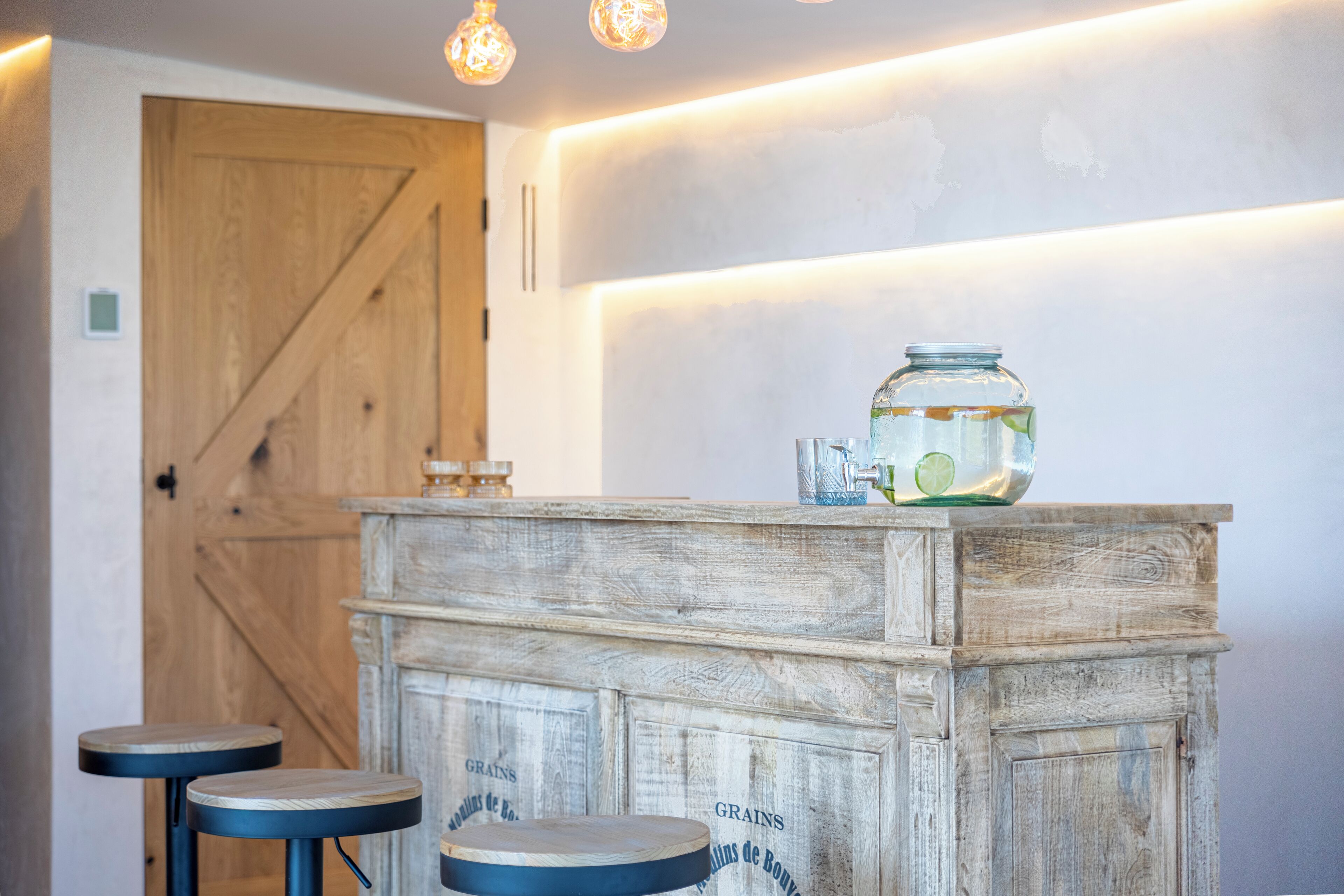 A rustic bar area with a wooden counter, two stools, and a jar of grains.
