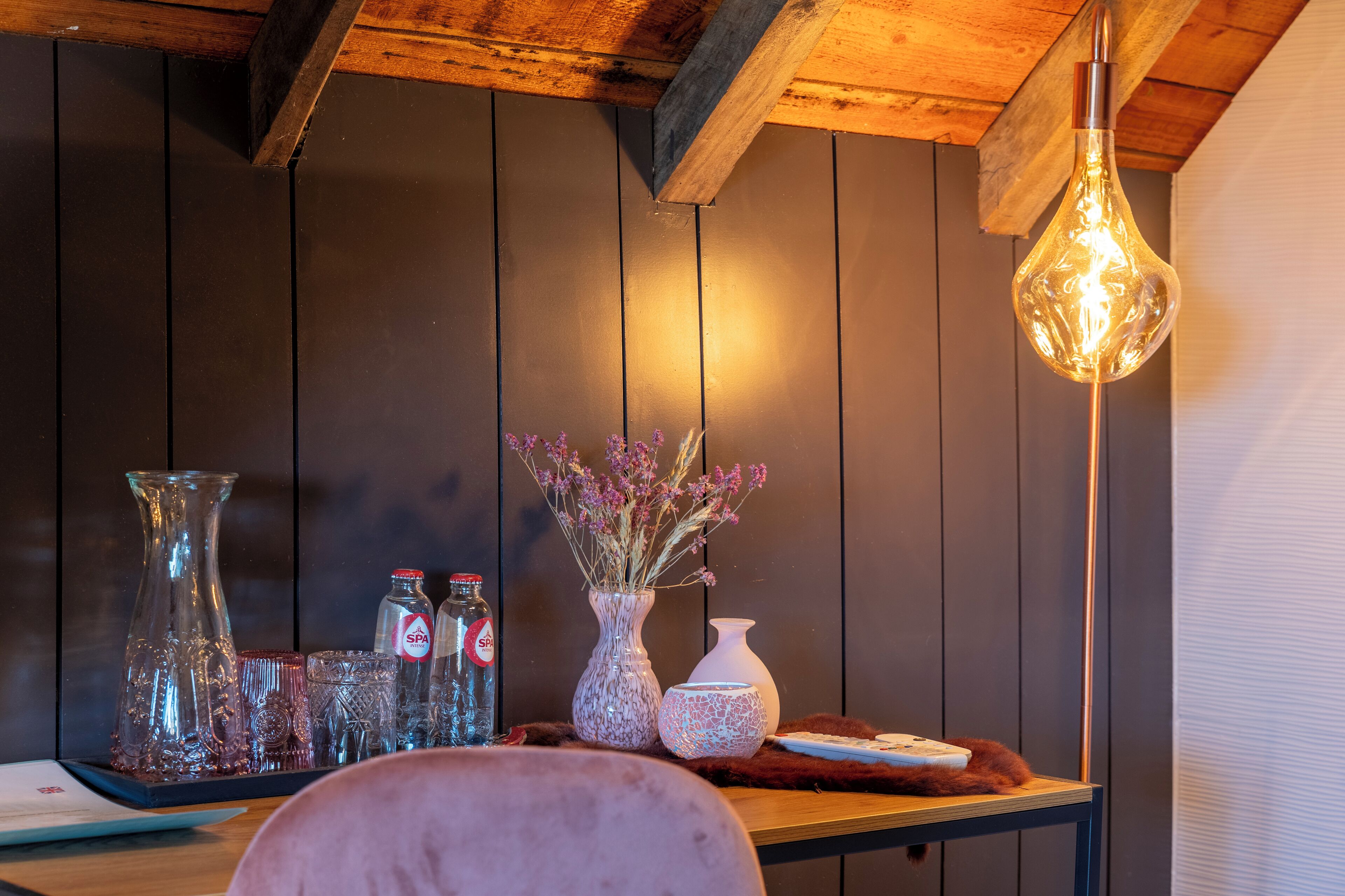 A wooden table with a vase of flowers, a bottle, and a candle.