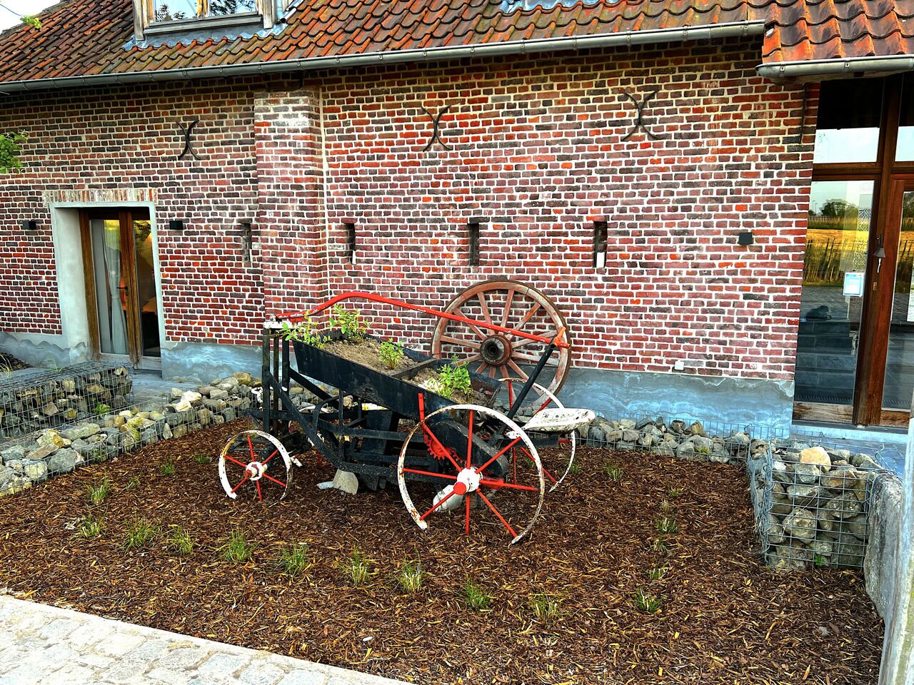 A brick building with a large wheel and a plow in the foreground.