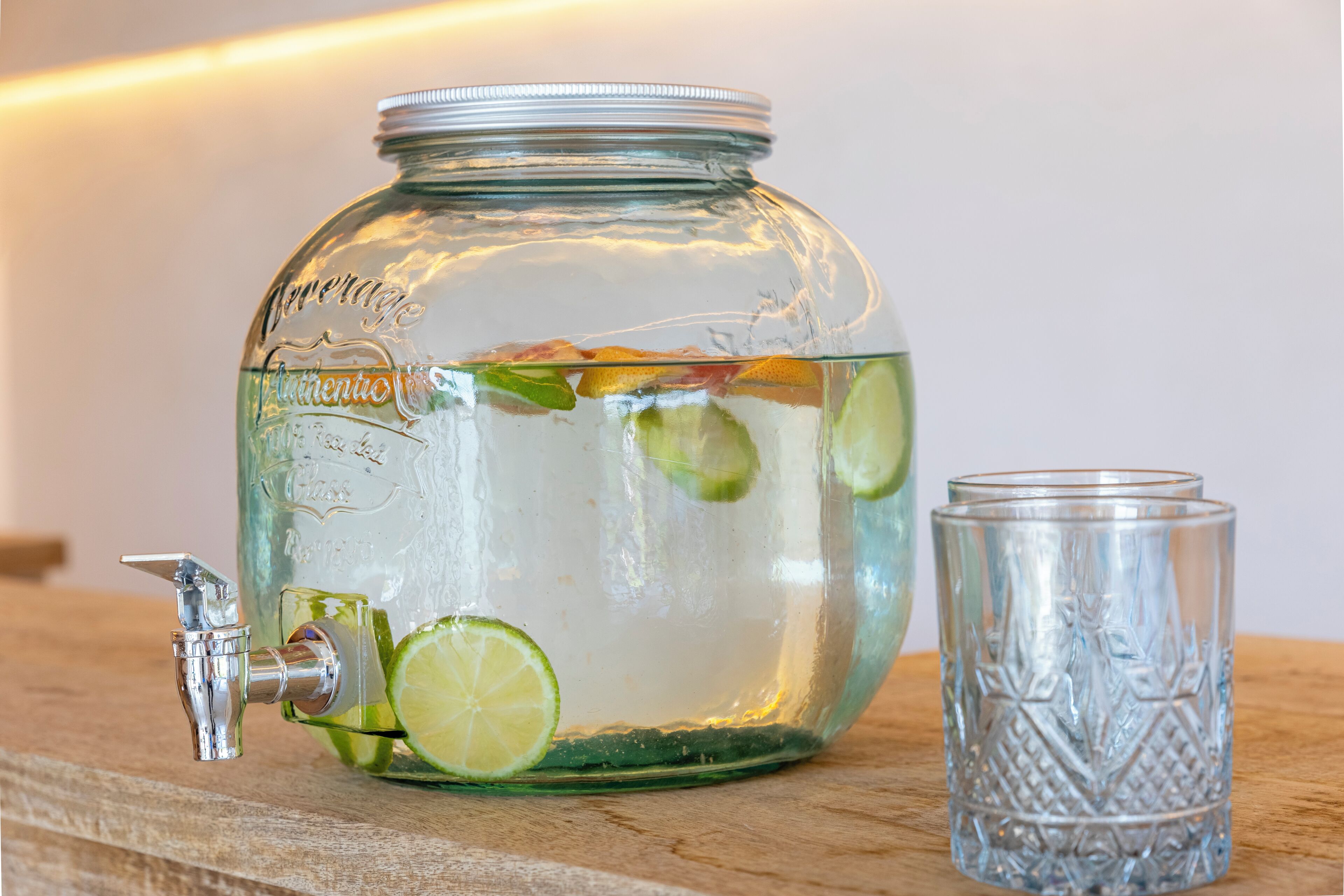 A glass jar with a tap and lime slices, next to a glass.