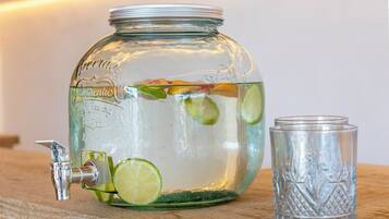 A glass jar with a tap and lime slices, next to a glass.