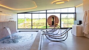 A modern spa room with a hot tub, two lounge chairs, and a large window offering a view of the outdoors. - Burgemeestershof (Wetteren)