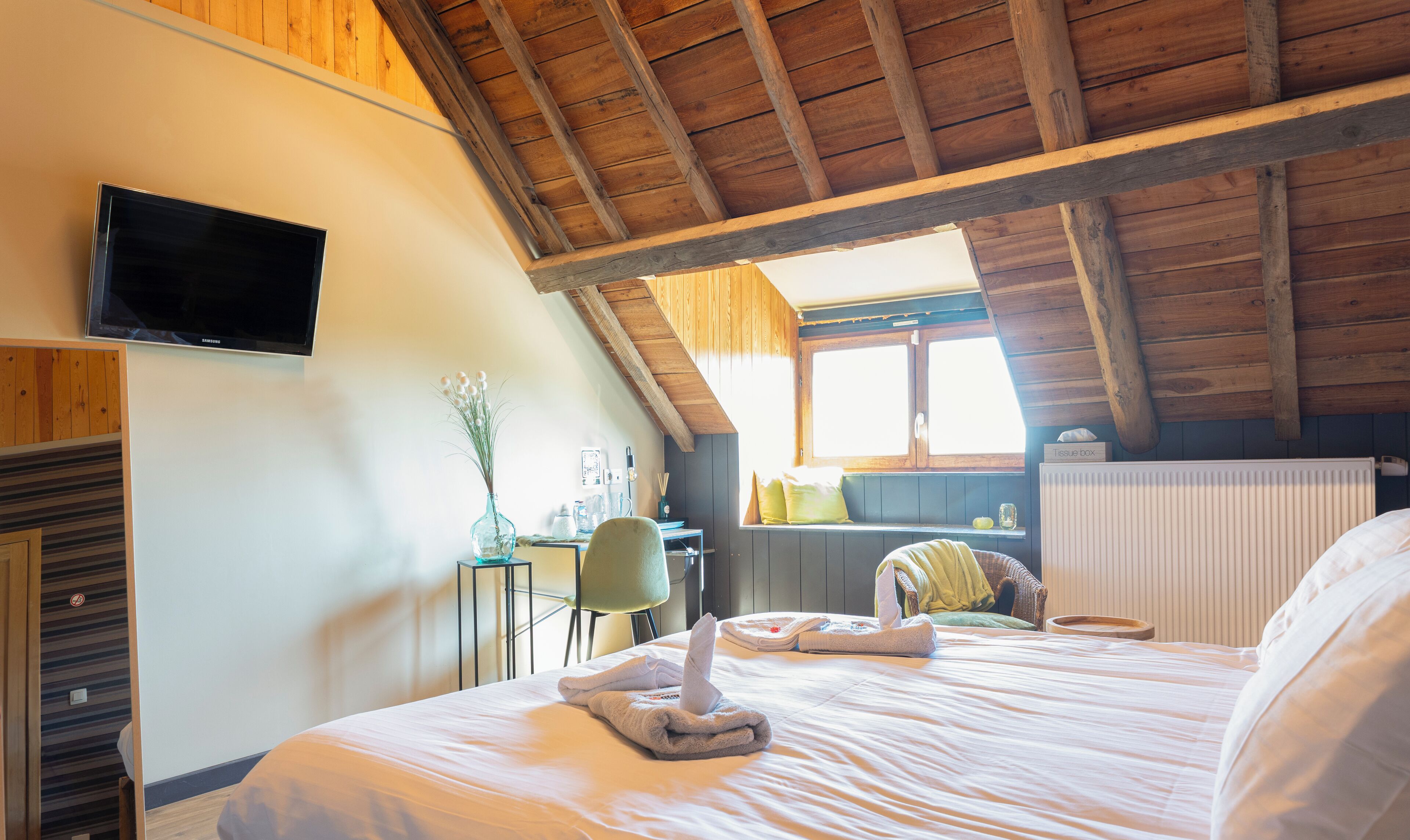 Un dormitorio con techo de madera, un televisor de pantalla plana en la pared, una cama con toallas, una silla y una ventana con vistas.