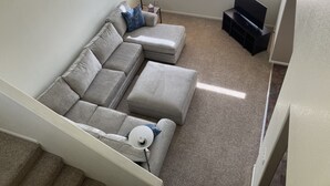Ein Wohnzimmer mit Ecksofa, Stehlampe, TV-Möbel und Deckenventilator.