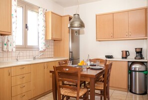 A kitchen with wooden cabinets, a stainless steel range hood, a dining table with chairs, and a trash bin.