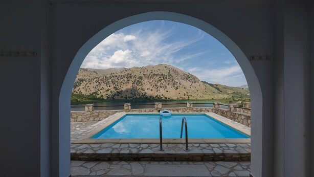 An outdoor swimming pool with stone tiles and metal railings, viewed through an arched doorway. - Linda's Villa In Unrivalled position in Kournas - Amazing View! (Kavallos)