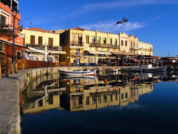 A waterfront area with buildings, a boat dock, and a reflection in the water.