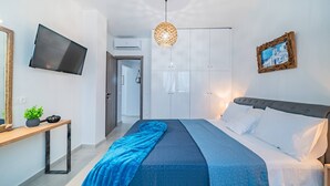 A bedroom with a bed, a TV mounted on the wall, a wooden bedside table, and a hanging light fixture.