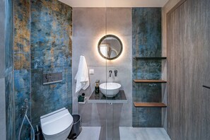 A modern bathroom with a white sink, a round mirror, and a towel rack. - Napoleon Navy Suite 1bd 1ba (Malia)