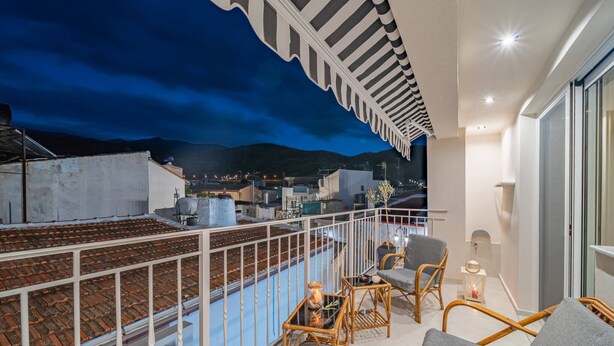 Ein Balkon mit Blick auf eine Stadtlandschaft im Abenddämmerung, mit Korbmöbeln und einem weißen Geländer.