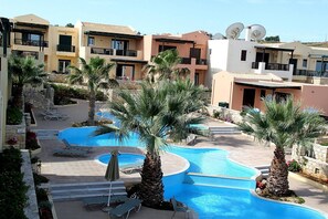 A resort with a swimming pool, palm trees, and modern buildings with balconies. - Nina's Place, 5min On Foot From The Beach (Panormos)