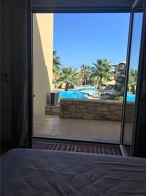 A room with a view of a swimming pool, palm trees, and a stone wall. - Nina's Place, 5min On Foot From The Beach (Panormos)
