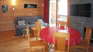 A cozy room with a wooden wall, a sofa, a dining table with chairs, and a TV mounted on the wall.