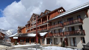 A multi-story wooden building with balconies, a ski lift, and a mountain backdrop.