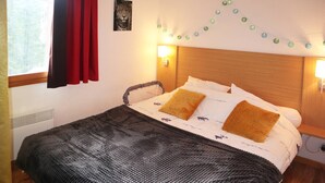 A neatly made bed with a patterned blanket, two pillows, and a headboard with wall-mounted lights.