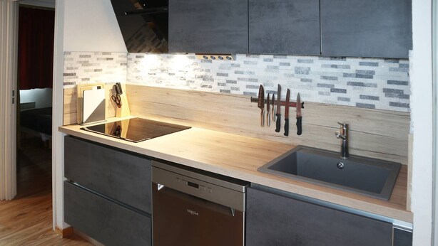A modern kitchen with a wooden countertop, a built-in dishwasher, and a tiled backsplash.