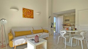 A bright living room with a yellow sofa, a white coffee table, and a dining area with white chairs. - Apartment T2 - 3 people - Air conditioning - Pool and tennis residence - Unobstructed view -... (STE MAXIME)