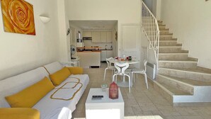 A modern living room with a sofa, coffee table, and a dining area with chairs and a table. A staircase leads to an upper floor. - Apartment T2 - 3 people - Air conditioning - Pool and tennis residence - Unobstructed view -... (STE MAXIME)