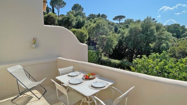 A balcony with a table set for two, white chairs, and a view of a lush green landscape. - Apartment T2 - 3 people - Air conditioning - Pool and tennis residence - Unobstructed view -... (STE MAXIME)