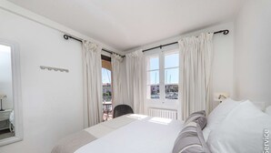 Une chambre avec un grand lit, une fenêtre avec des rideaux, une vue sur l’extérieur et une petite table avec une chaise.