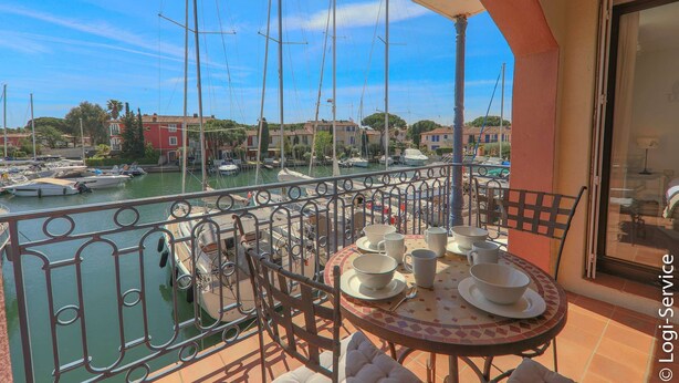 Un balcon avec une table dressée pour le dîner, donnant sur une marina où l’on peut admirer des bateaux et des bâtiments.