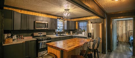 A modern kitchen with dark cabinetry, stainless steel appliances, and a wooden island with bar stools.