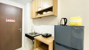 A compact kitchen with a sink, wooden cabinets, a black refrigerator, and a yellow appliance on top. - Chic And Cozy Studio Apartment At Transpark Juanda Bekasi (Bekasi)