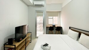 A hotel room with a bed, a TV on a wooden stand, a desk with two chairs, and an air conditioning unit. - Chic And Cozy Studio Apartment At Transpark Juanda Bekasi (Bekasi)