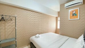 A neatly made bed with white linens and two rolled towels, a metal shelf unit, and a wall-mounted air conditioner. - Comfort And Elegant 4Br Combined At Springlake Summarecon Bekasi Apartment (Bekasi)