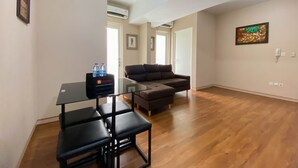 A living room with a glass-top dining table, two black chairs, a brown sectional sofa, and a water dispenser. - Comfort And Elegant 4Br Combined At Springlake Summarecon Bekasi Apartment (Bekasi)