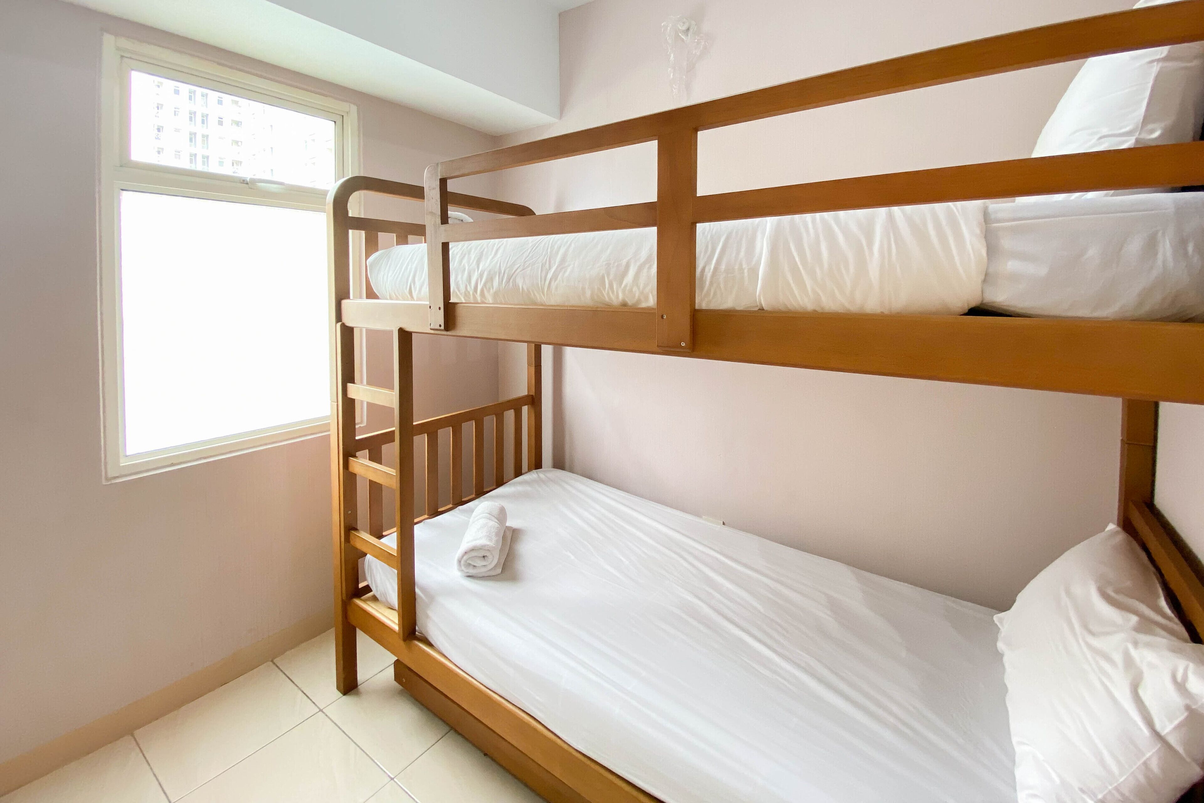 A bunk bed room with a window, white bedding, and a tiled floor.