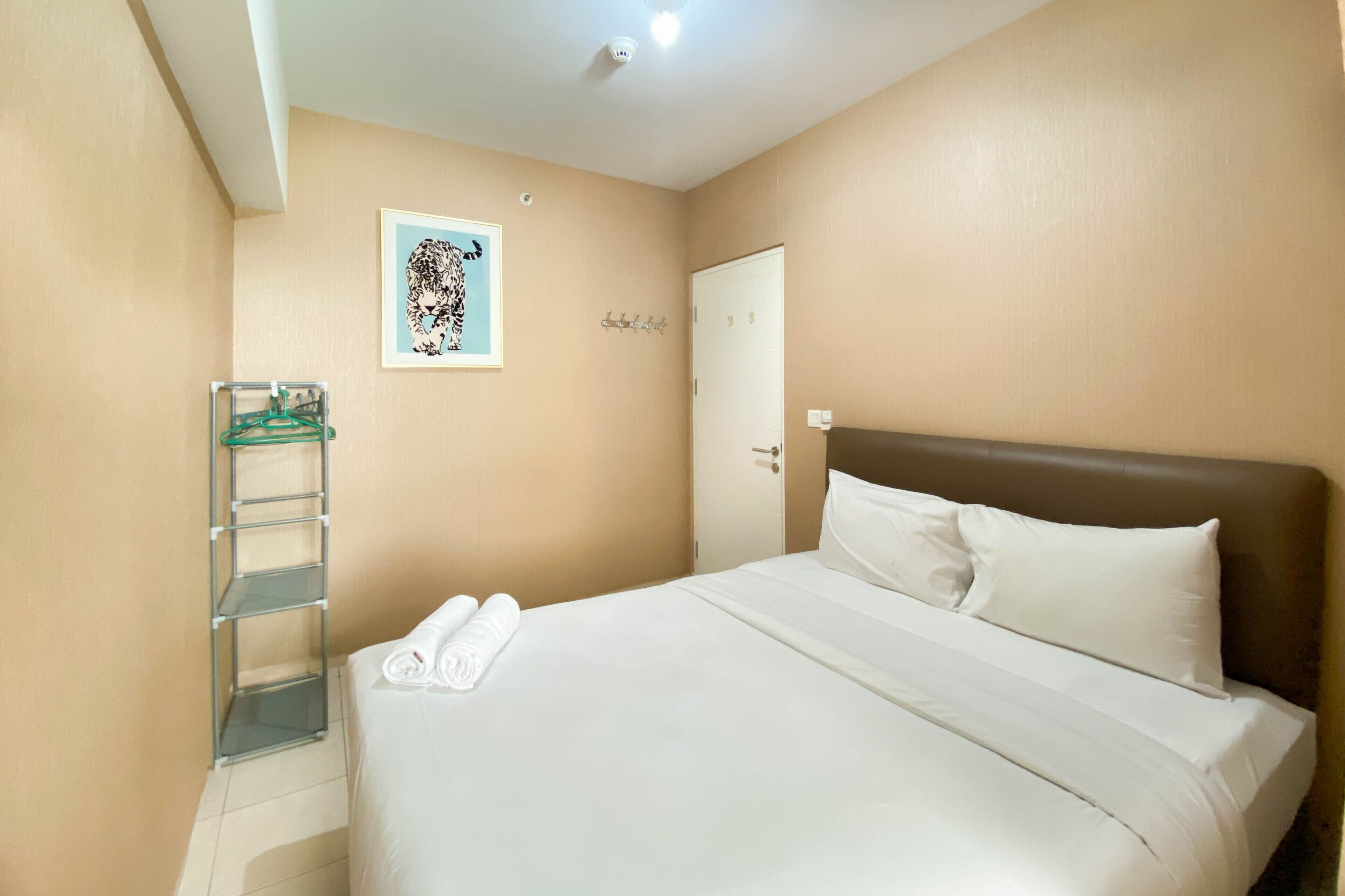 A hotel room with a bed, a wall-mounted shelf, a door, and a framed picture.
