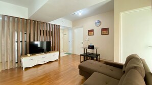 A modern living room with a flat-screen TV on a white cabinet, a brown sofa, and a wooden partition. - Comfort And Elegant 4Br Combined At Springlake Summarecon Bekasi Apartment (Bekasi)