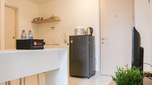 A compact kitchen with a white countertop, a refrigerator, a sink, and a shelf above the countertop holding kitchenware.