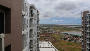 A high-rise building with multiple balconies overlooking a coastal area with a view of the sea and a distant shoreline.